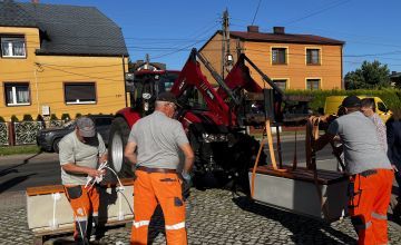 Koparka i kilka osób wokół ustawiających ławkę w odpowiednim miejscu